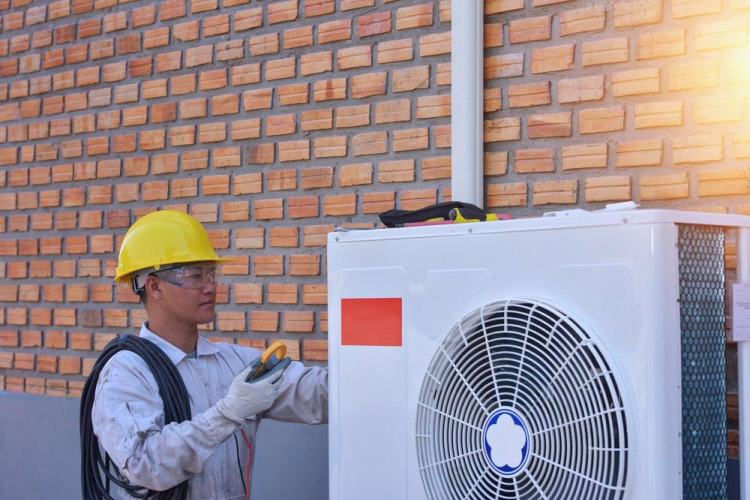 Technician inspecting an outdoor air cooler unit against a brick wall in the UAE